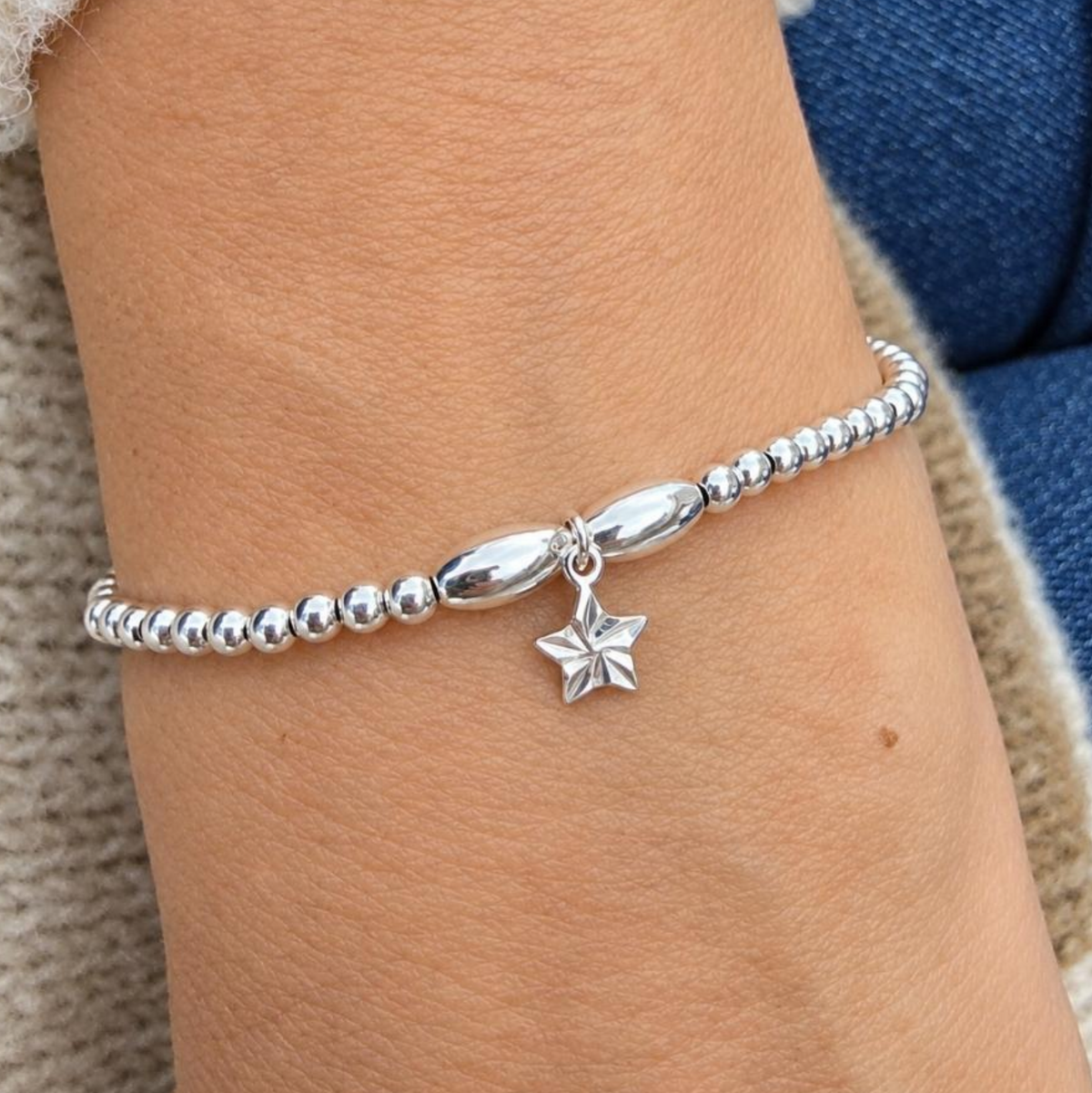 A close-up of a delicate silver beaded bracelet with a polished star charm, worn on a person's wrist.