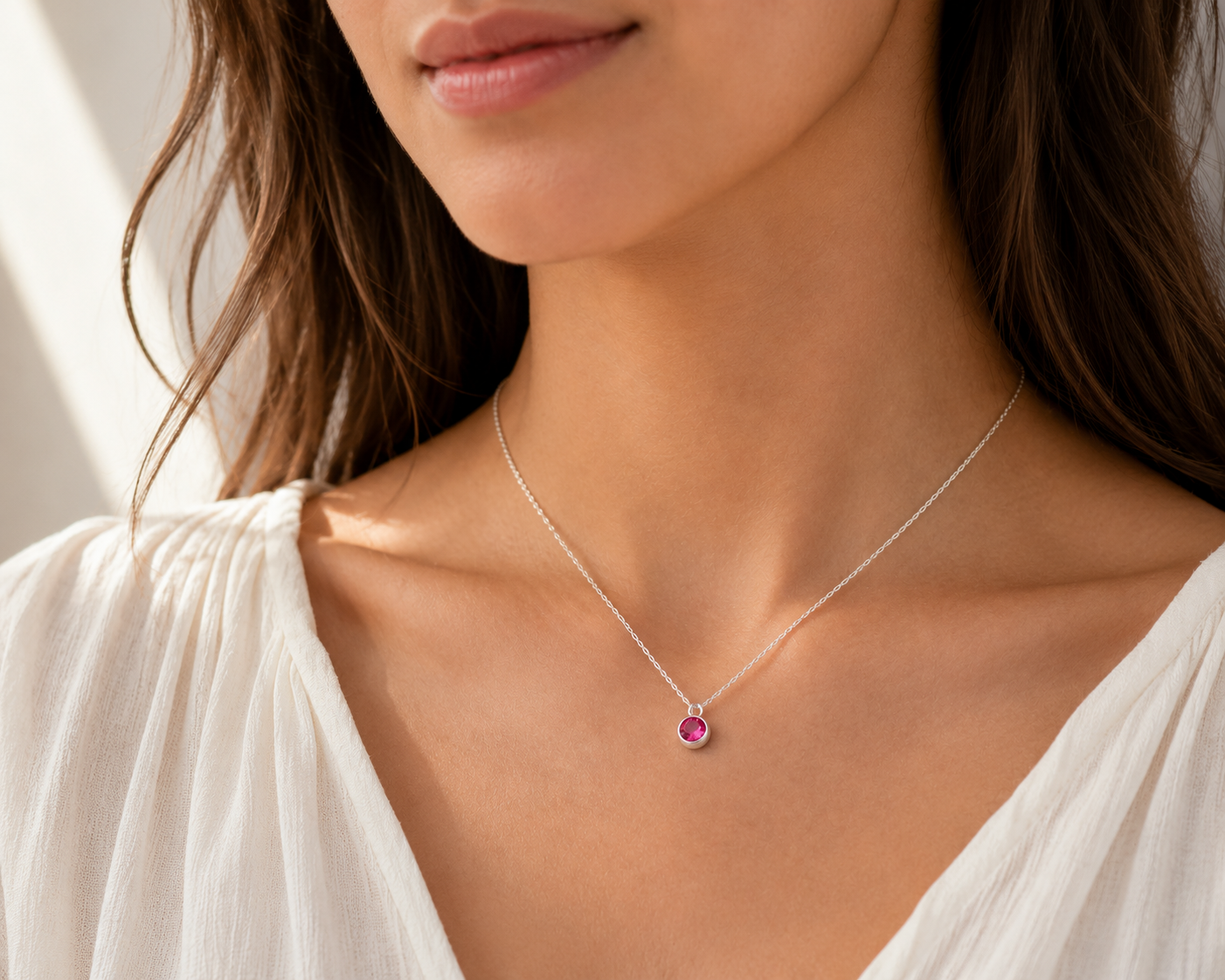 Close-up of a woman wearing a silver necklace with a pink gemstone pendant.