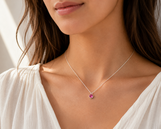 Close-up of a woman wearing a silver necklace with a pink gemstone pendant.