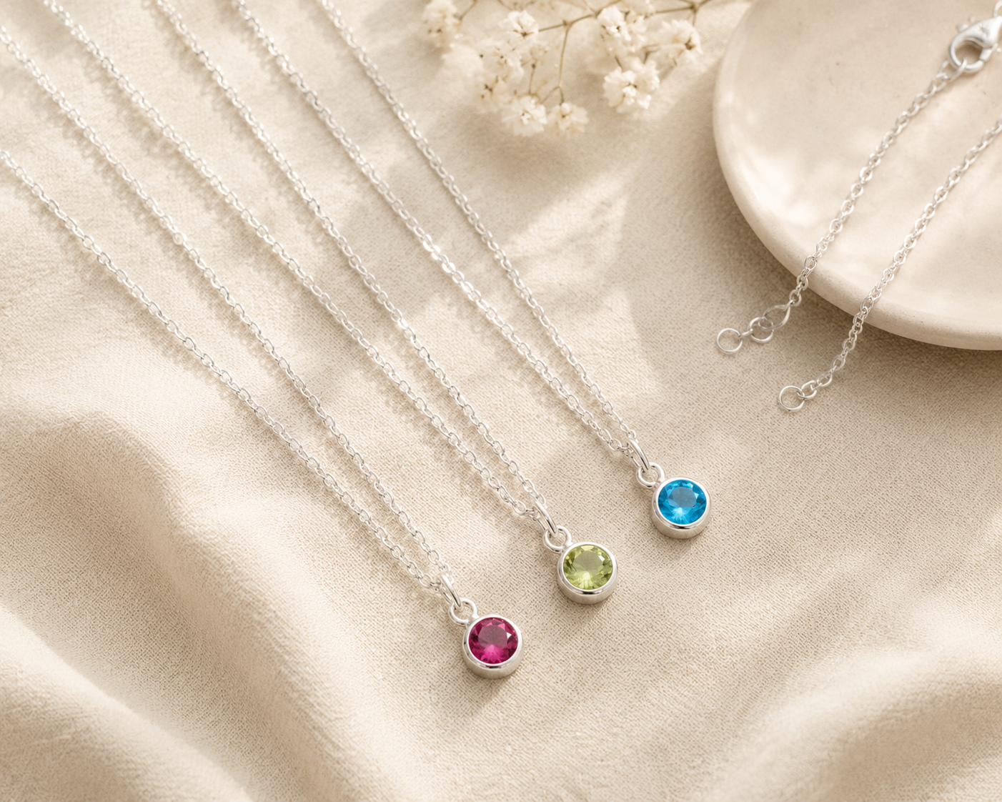 Three silver necklaces with colorful gemstones on a beige fabric background