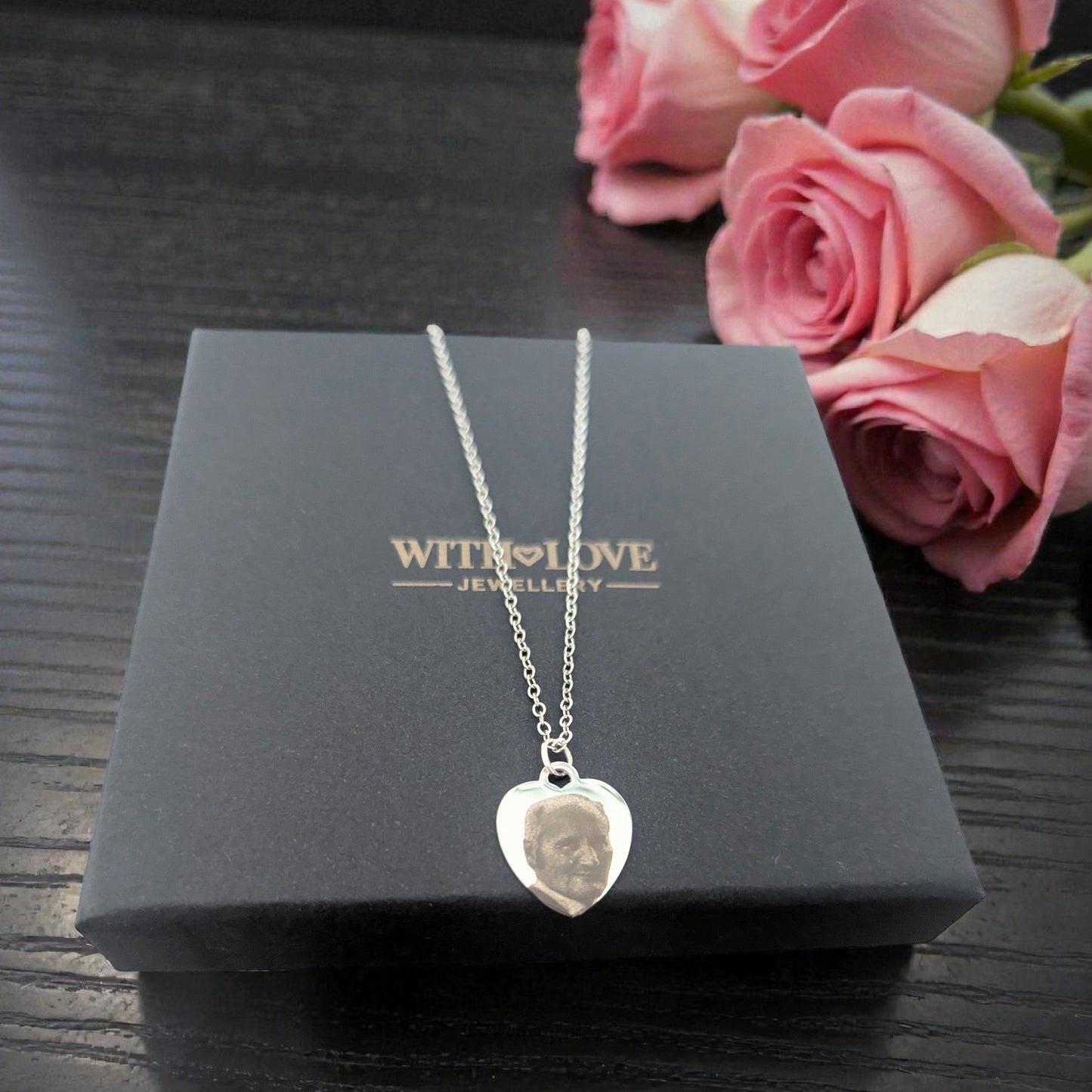 Silver heart-shaped pendant necklace on a black box with pink roses in the background