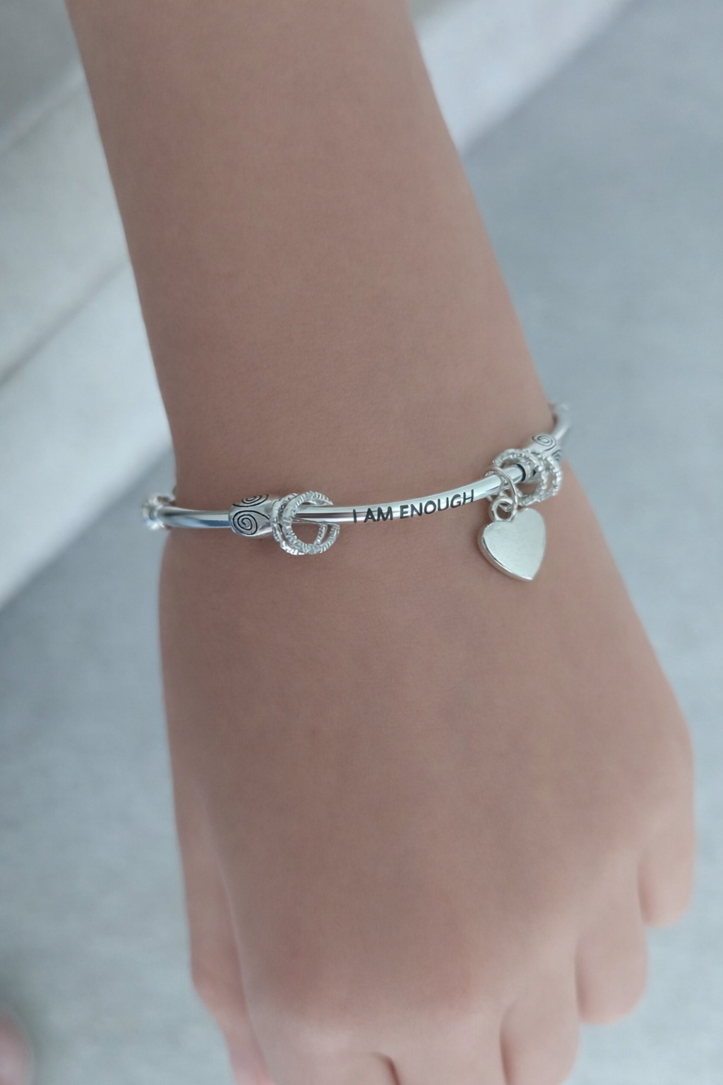 Silver bracelet with heart charm on a wrist against a light background