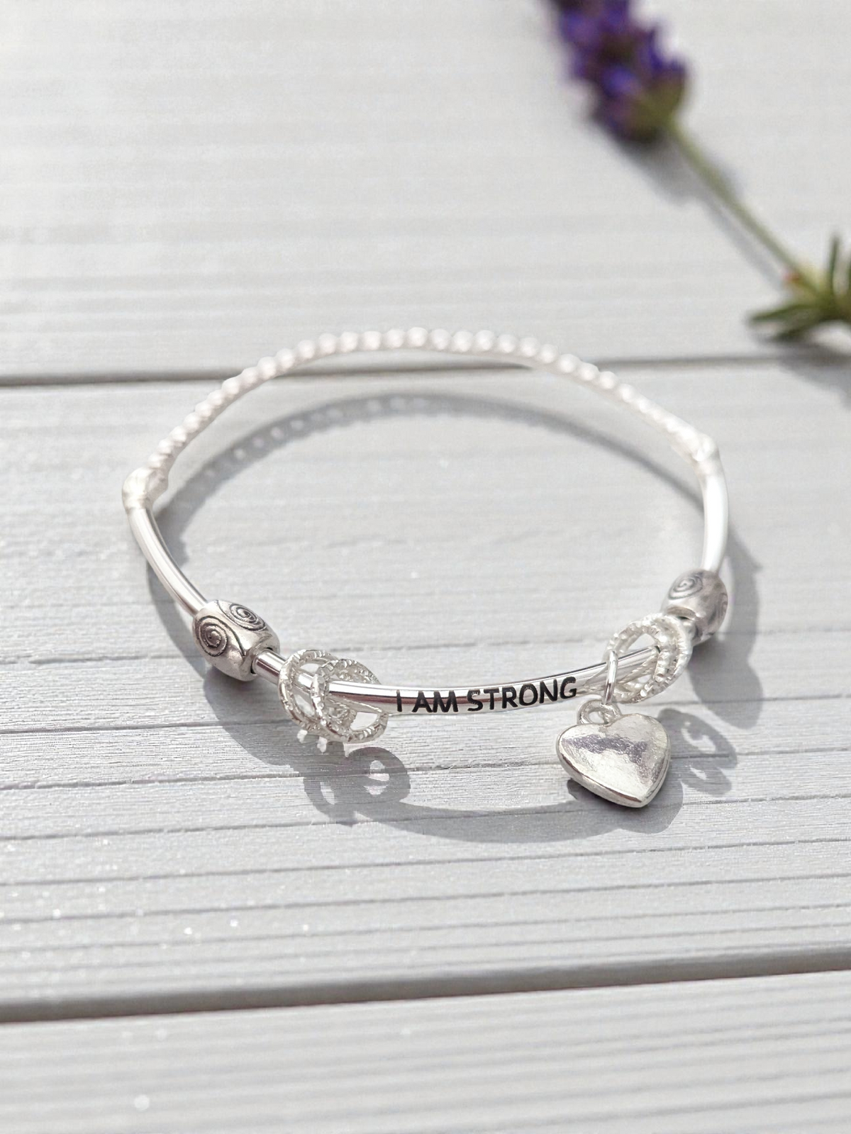 Silver bracelet with 'I AM STRONG' message on a wooden surface with lavender flowers.