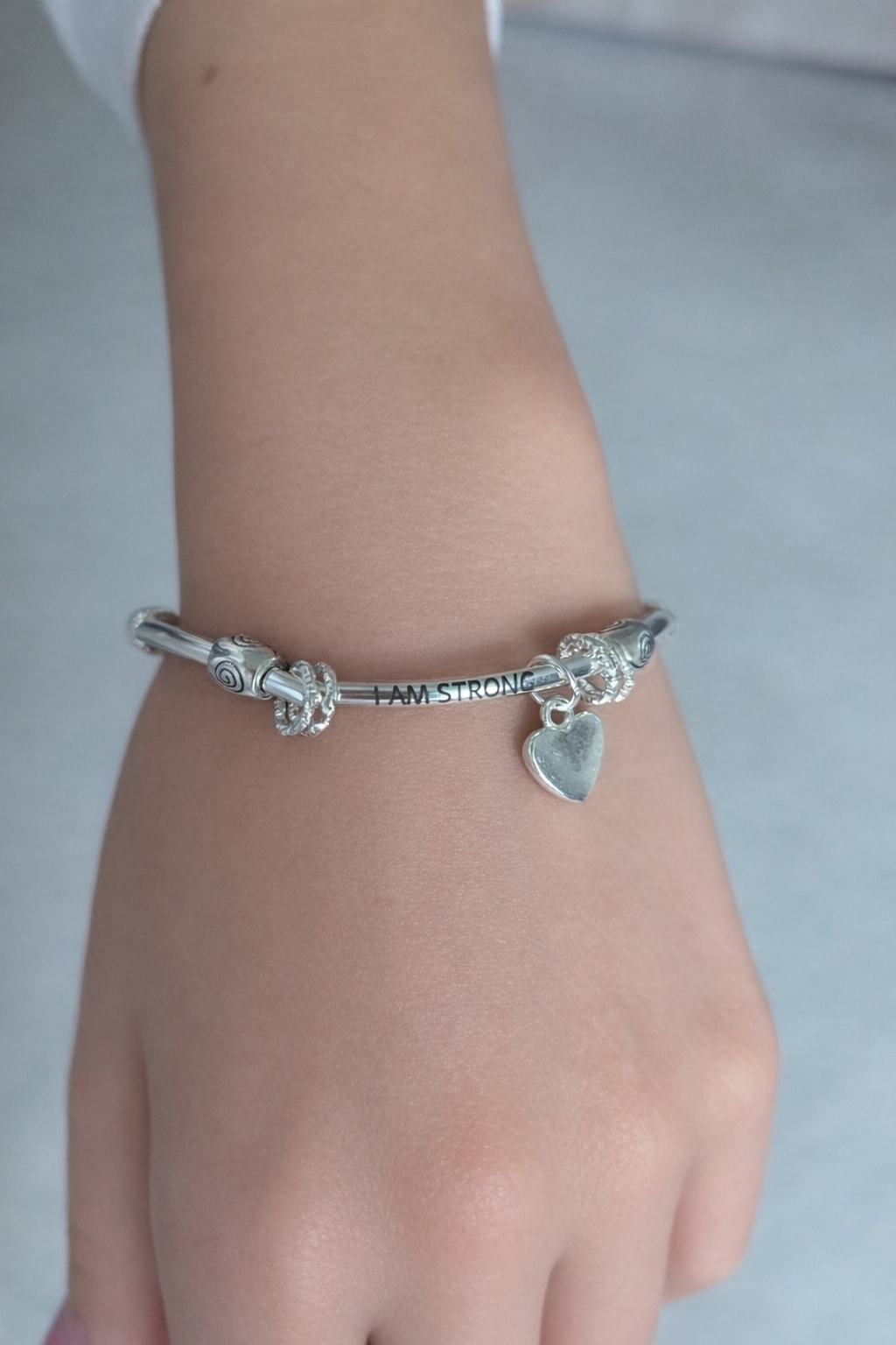 Silver bracelet with charms on a wrist against a neutral background