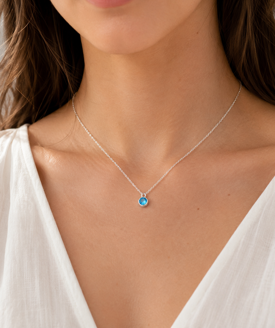 Necklace with a blue pendant worn by a person in a white top