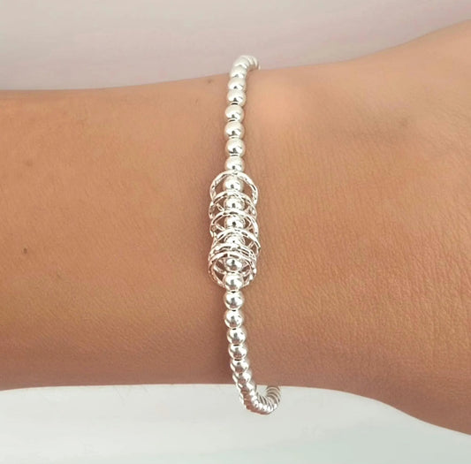 A silver beaded bracelet with a central textured woven or mesh-like cluster, shown worn on a person's wrist.