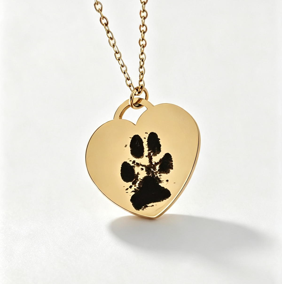 A gold heart-shaped pendant necklace featuring a black paw print design, suspended from a delicate gold chain against a clean white background.