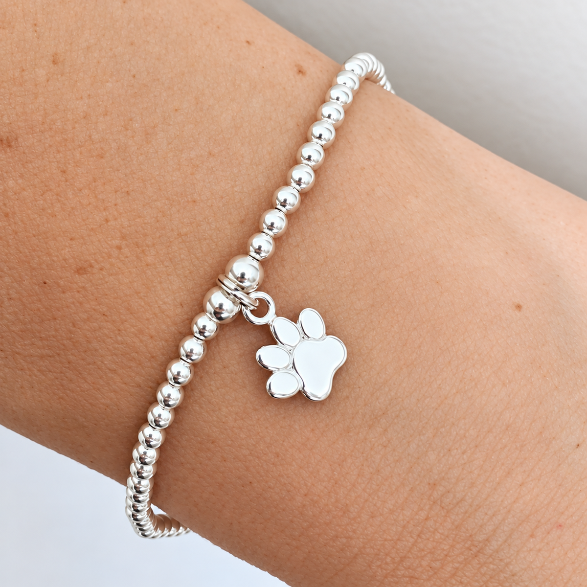 A silver beaded bracelet with a paw print charm, shown worn on a person's wrist.