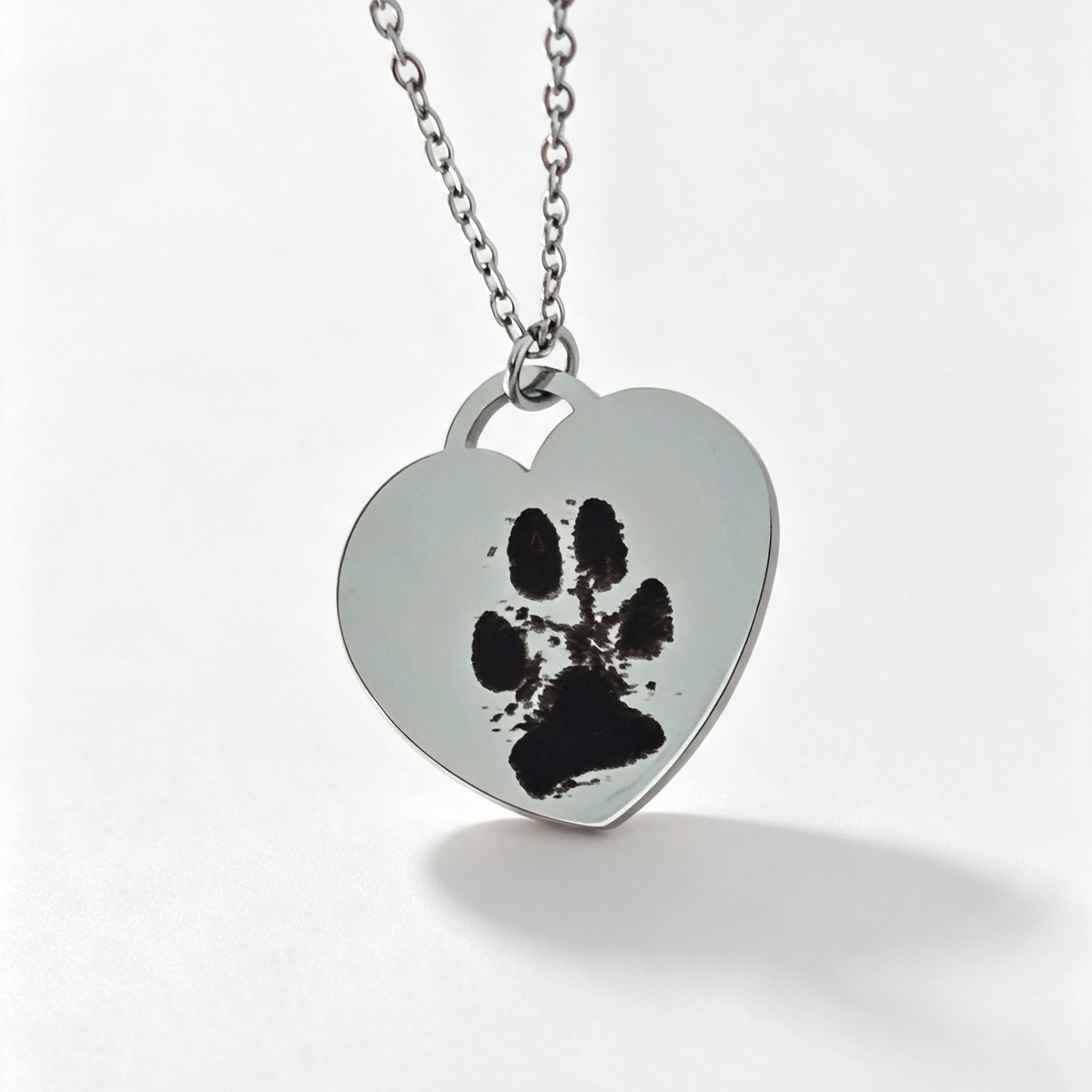 A silver heart-shaped pendant necklace with a black paw print design, hanging on a silver chain against a white background.