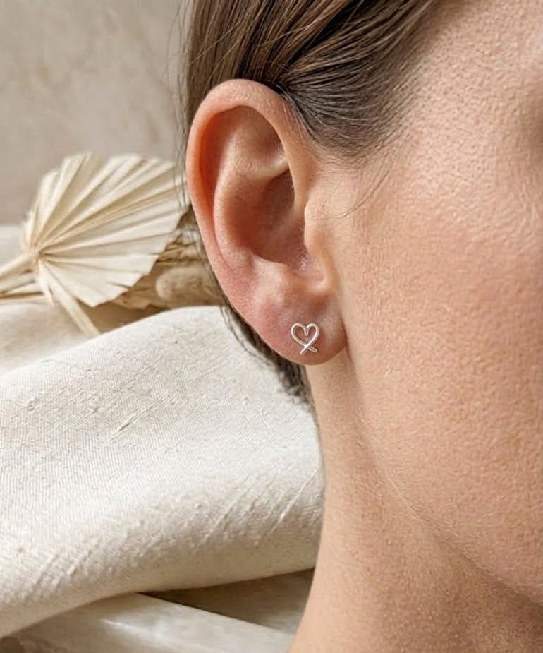 Close-up of an ear wearing a heart-shaped earring with a neutral background